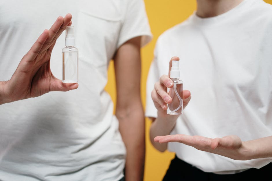 Two people in white shirts holding sanitizer bottles against a yellow backdrop.