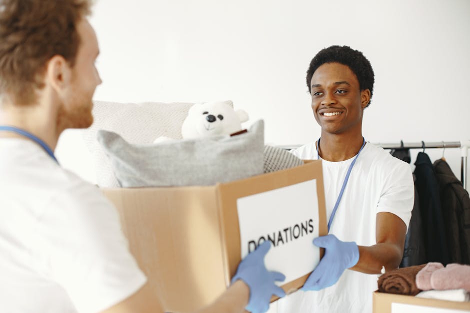 Two volunteers joyfully handing and receiving donation boxes full of clothes and toys.